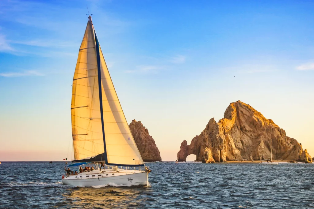 A sailing boat passes the Land’s End rocks in warm low evening light.