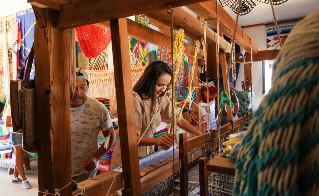 Looms and hanging woven goods fill a long open weaving workshop.