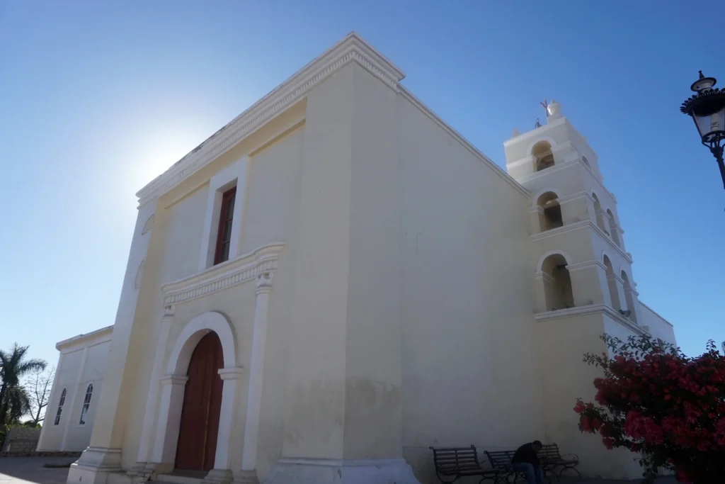 A white mission church with a bell tower stands against a clear blue sky.