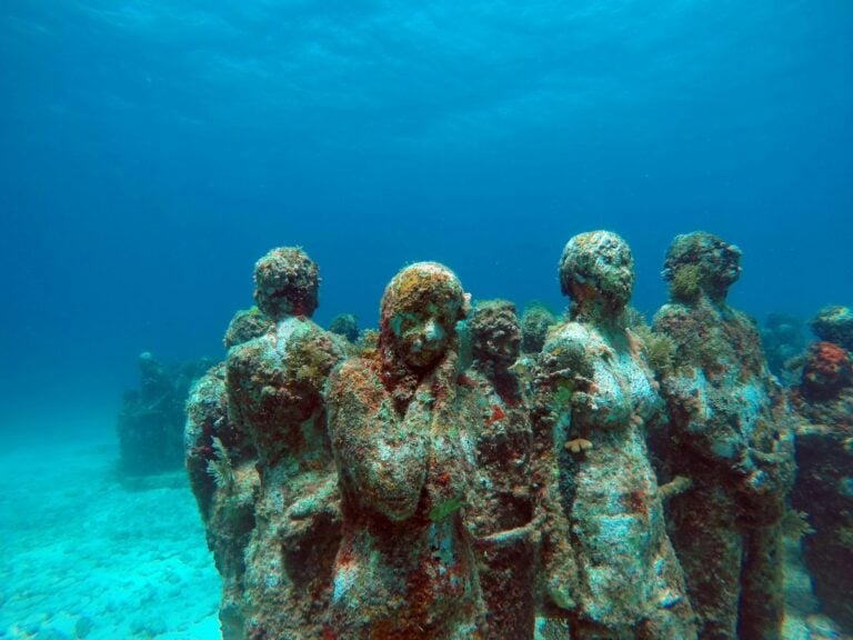 Coral-covered human sculptures of the MUSA underwater museum on the seabed in clear blue water