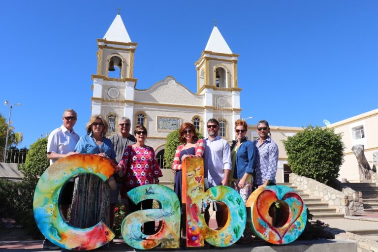Tour group posing behind the colorful "Cabo" letters in front of the San José del Cabo mission church