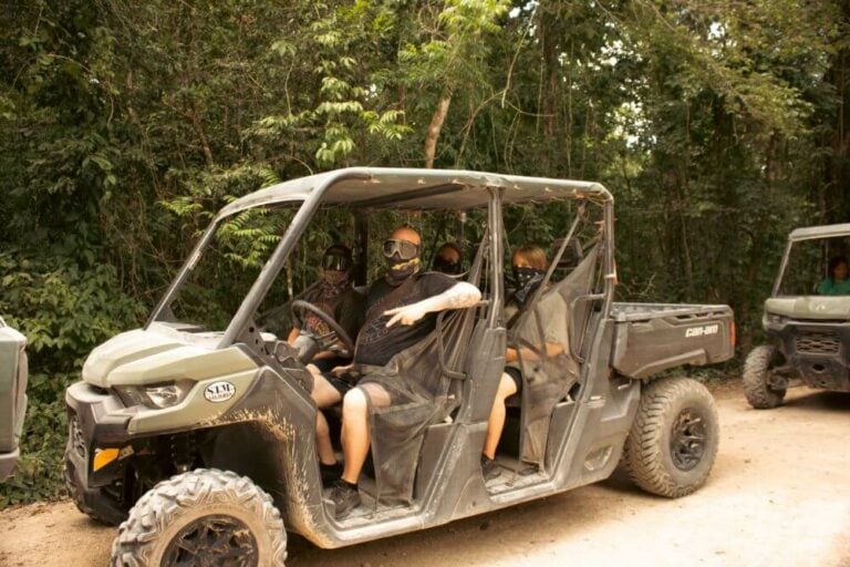 Guests in face masks sit in an off-road buggy on a dirt jungle track, with a second buggy behind them