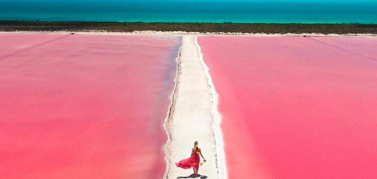 A woman in a red dress walks along a white path between the bright pink salt lakes of Las Coloradas