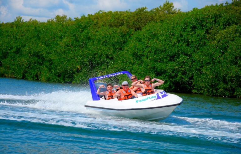 A small speedboat carrying guests in orange life vests races across the lagoon past green mangroves