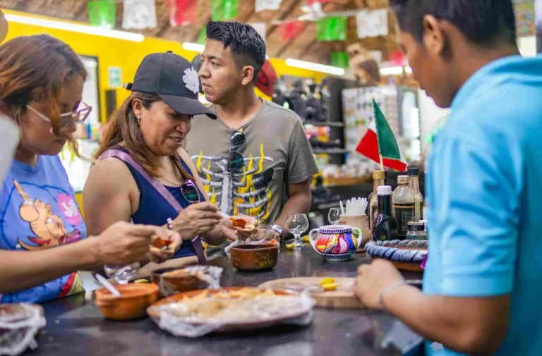 Guests sampling Oaxacan dishes in small clay bowls at a colorful local food stall during the city tour