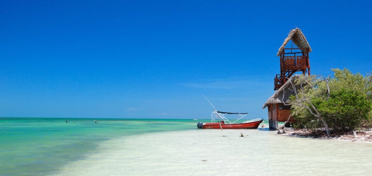 A thatched lookout tower and a small boat on the white sand and shallow water of Isla Pasion