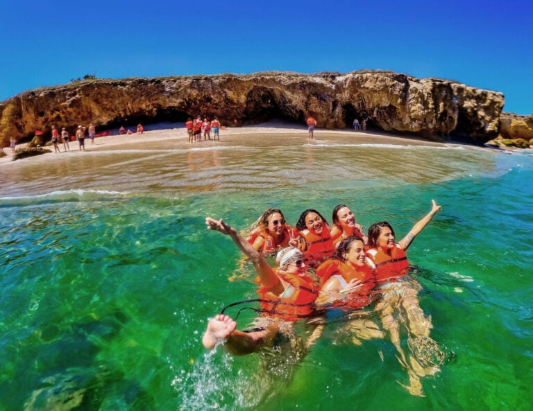 Group in orange life jackets swimming in green water off a Marietas Islands beach below the rock formations