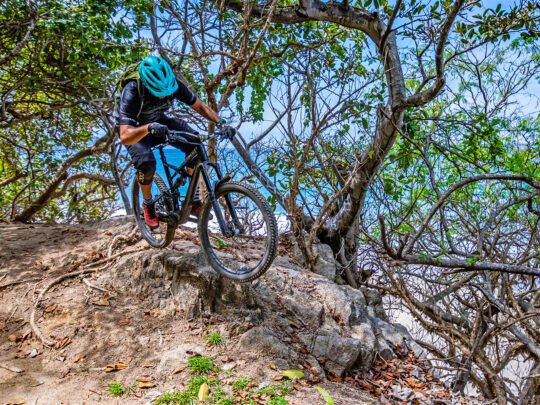 Mountain biker in blue helmet riding down a rocky jungle trail near Sayulita