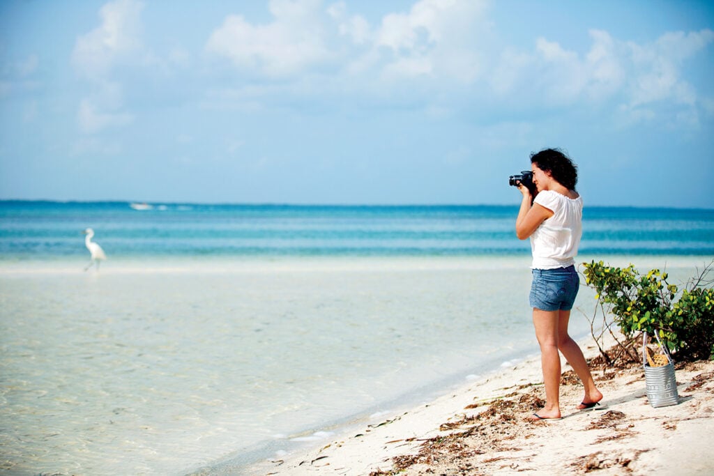Visitor photographing the shallow turquoise water and white sand at Isla Pasión