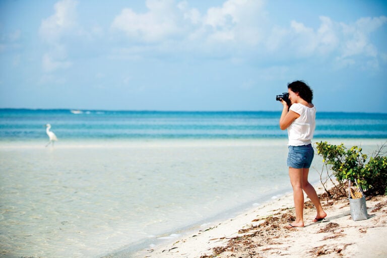 Visitor photographing the shallow turquoise water and white sand at Isla Pasión