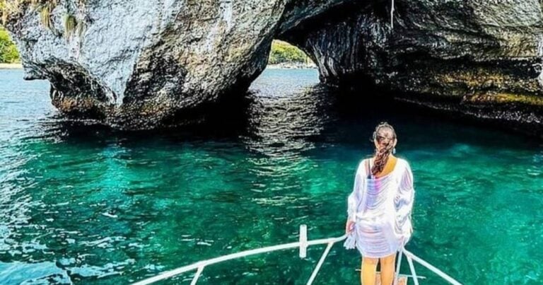 Guest on a boat bow inside a Los Arcos rock arch over turquoise water
