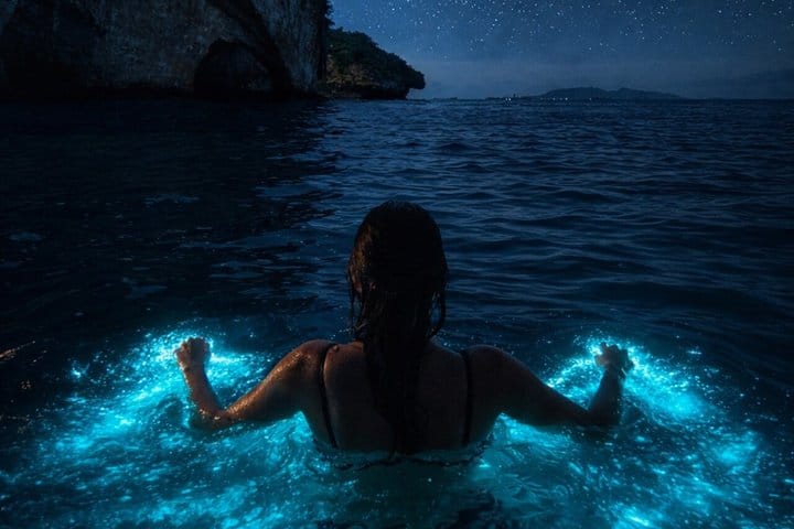 Swimmer glowing in bioluminescent water at night near Los Arcos
