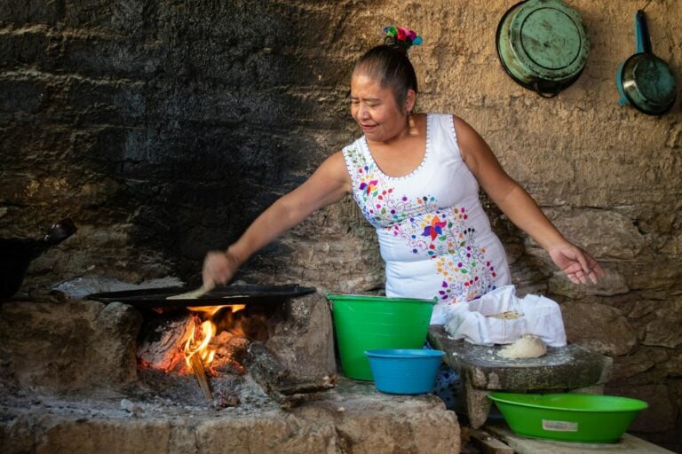 A traditional Mexican cook making tortillas on a comal over a wood fire in a rustic kitchen