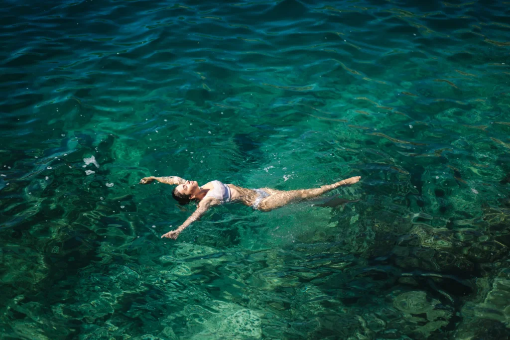 A guest floats on their back in clear green water seen from above.