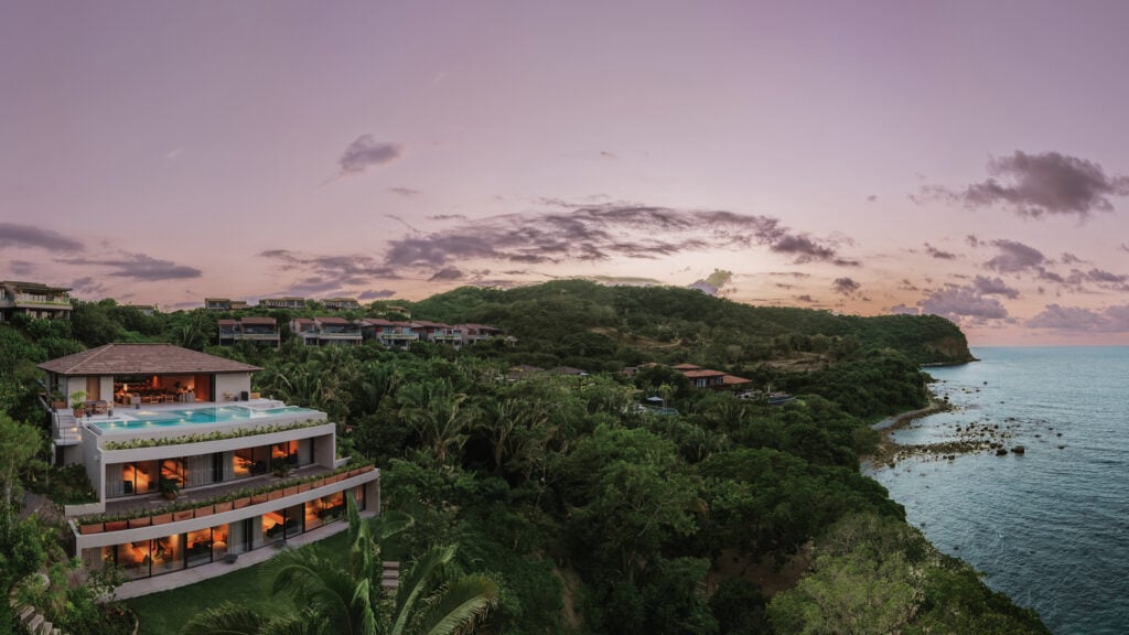 Villa Taiyari lit at dusk on the hillside above the coast, the pool glowing on its top terrace — Punta Mita Nayarit, Mexico