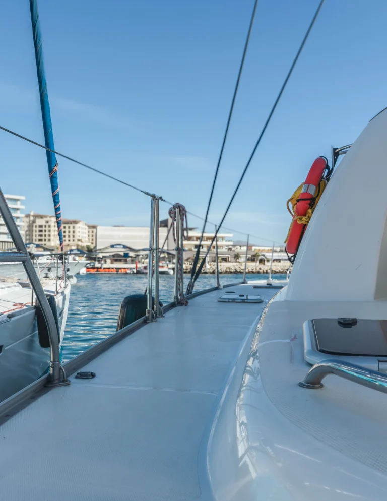 A view along the side deck of a sailing catamaran towards the bow, under sail.