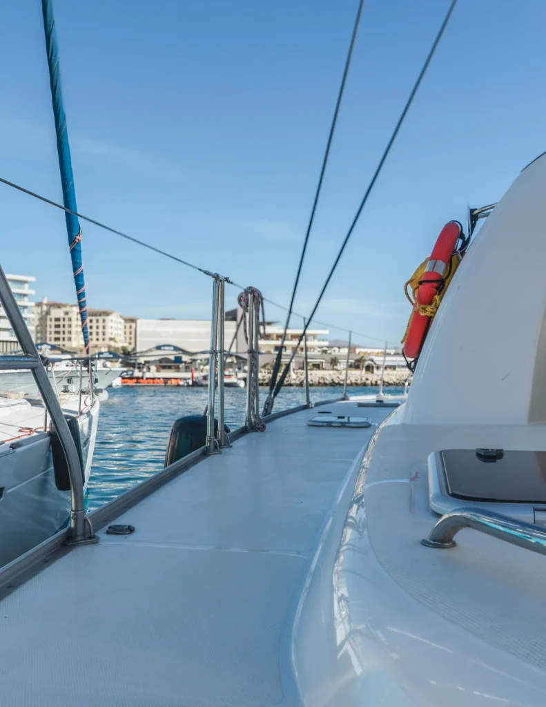 A view along the side deck of a sailing catamaran towards the bow, under sail.