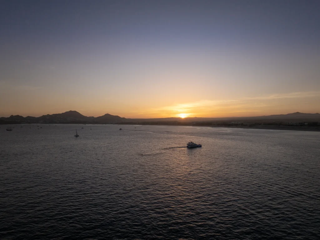 The sun sits low over open water with a boat small on the horizon.